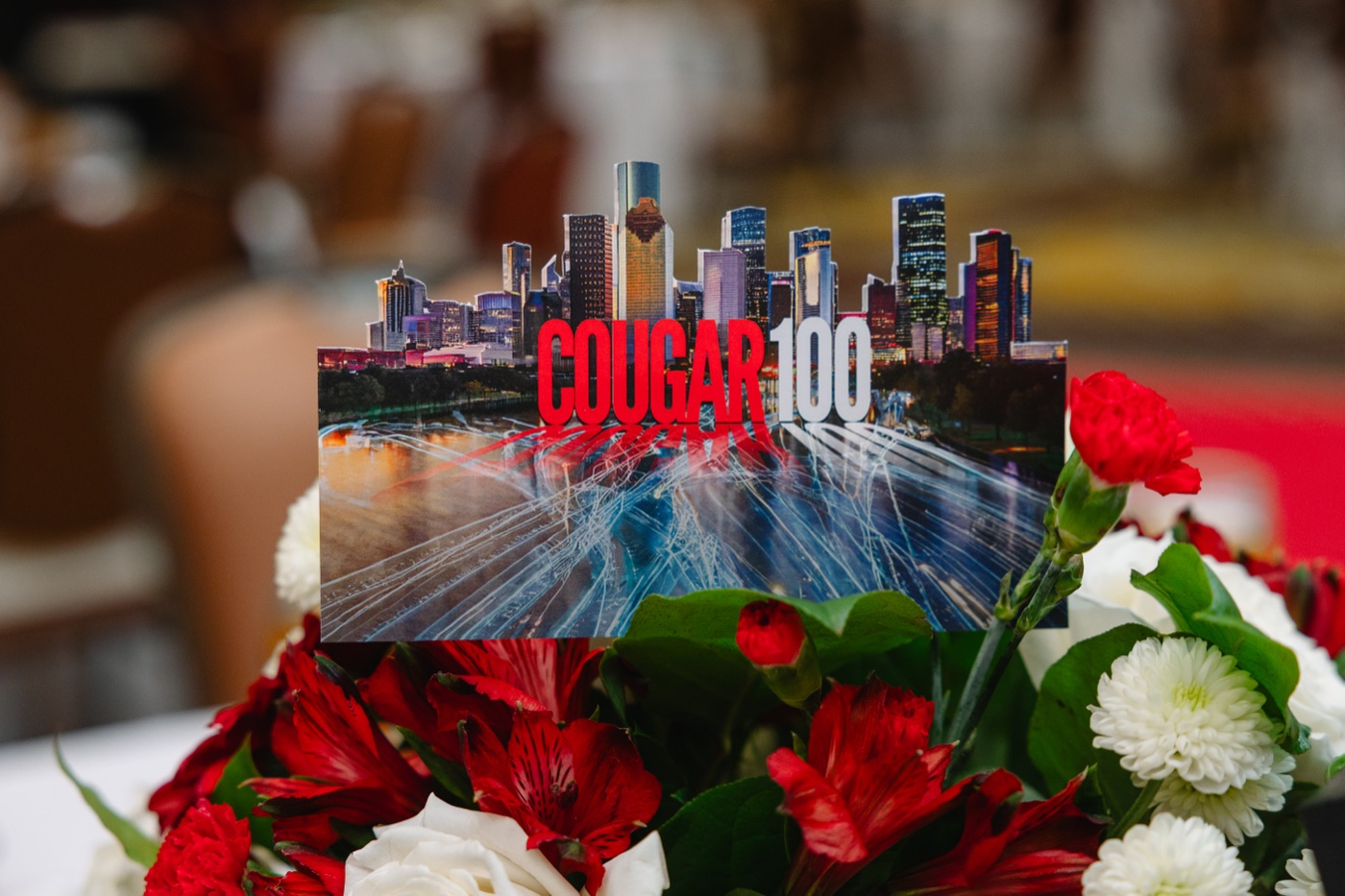 Cougar 100 table card with Houston skyline graphic, set in a red and white floral centerpiece