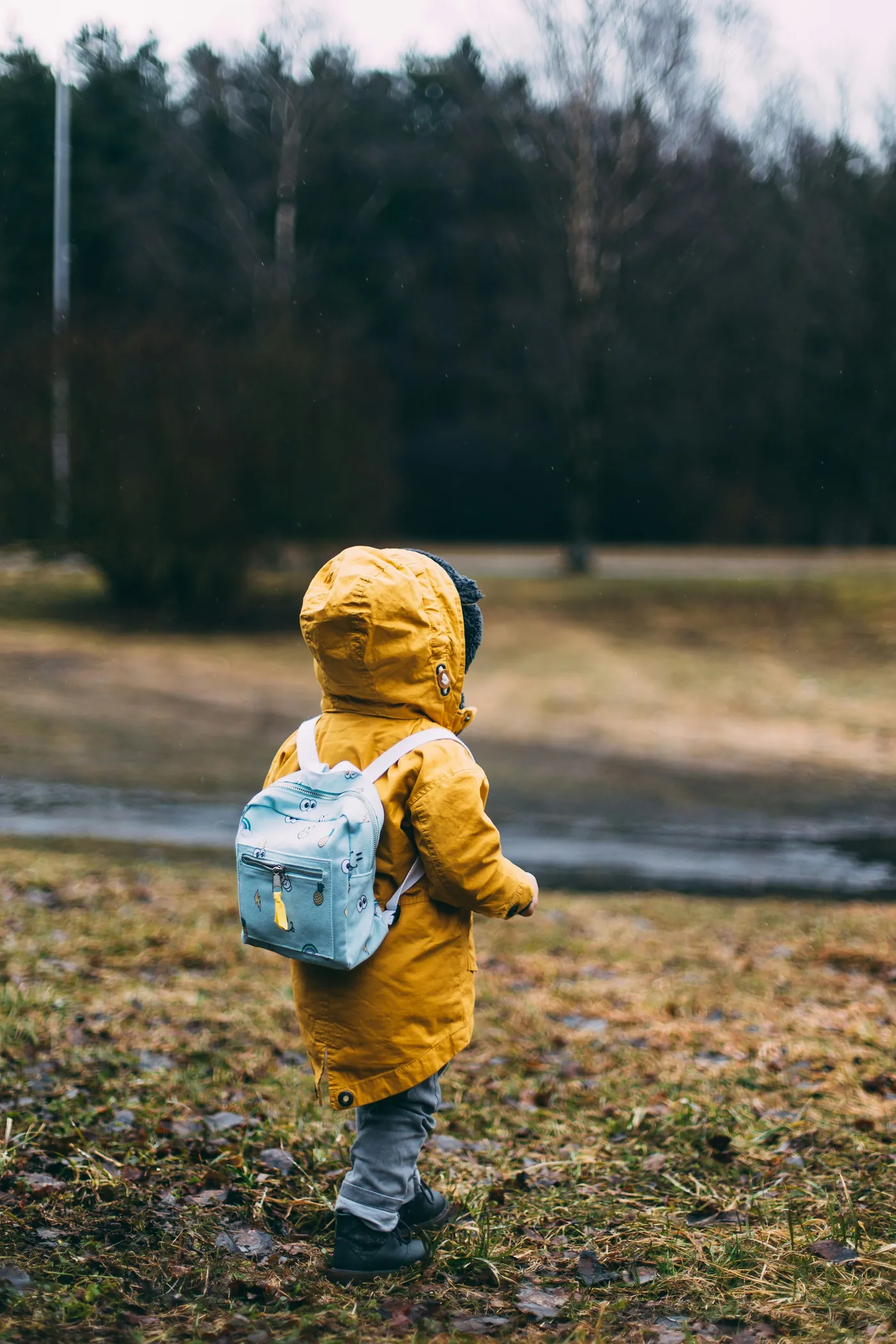 A small child in a yellow raincoat and backpack walking along a path