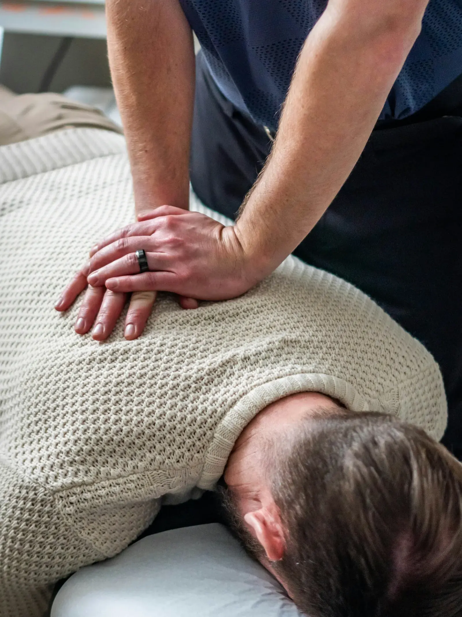 A chiropractor with both hands on a patient's upper back during an adjustment