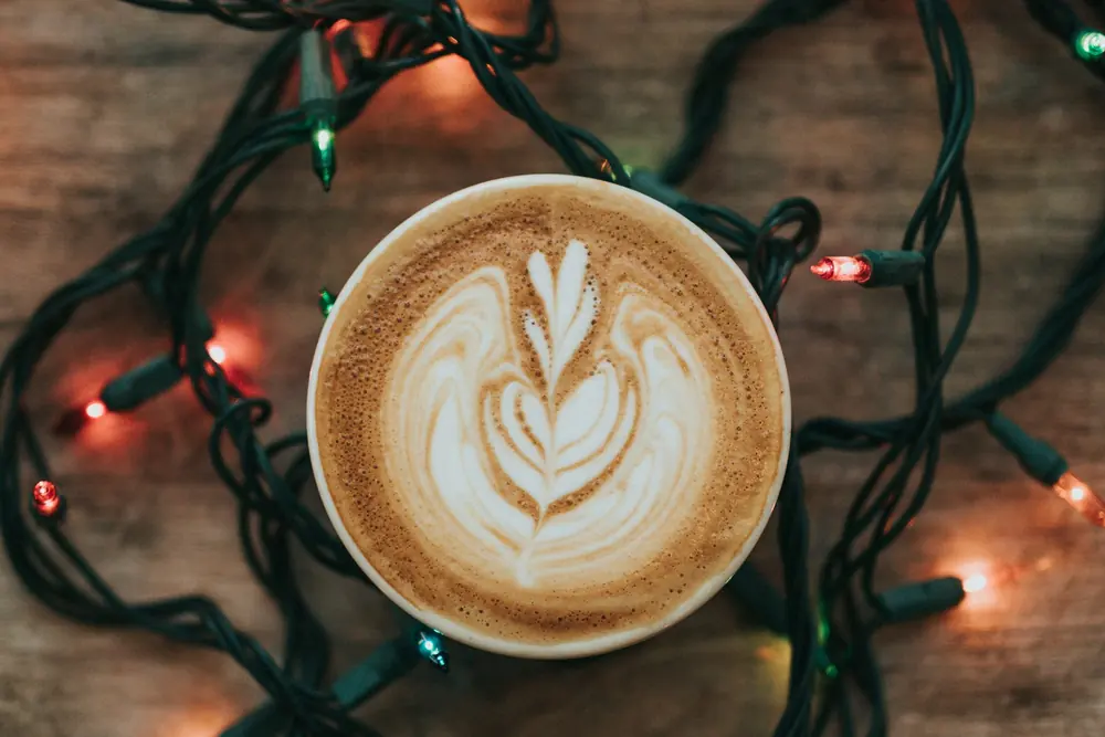 A latte with leaf art beside a string of fairy lights