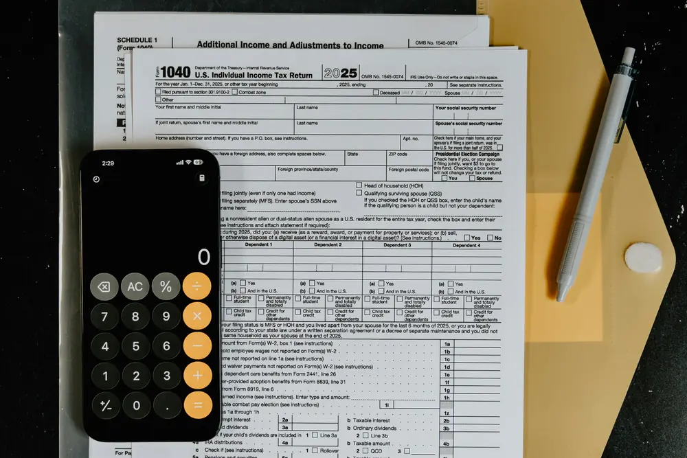 A Form 1040, a phone calculator and a pen on a dark desk