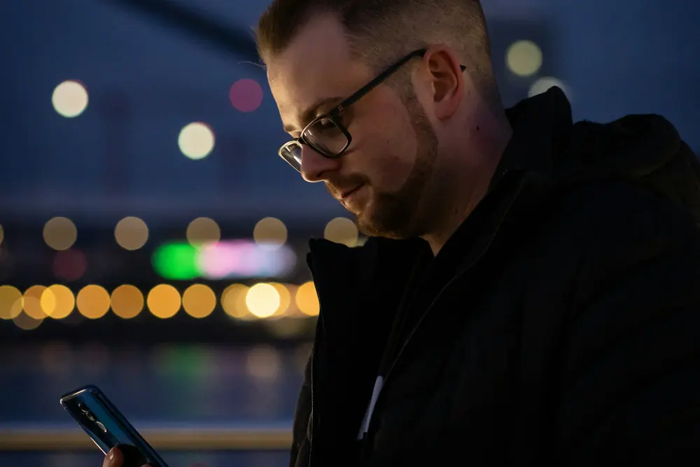 A man reading his phone at night by the water