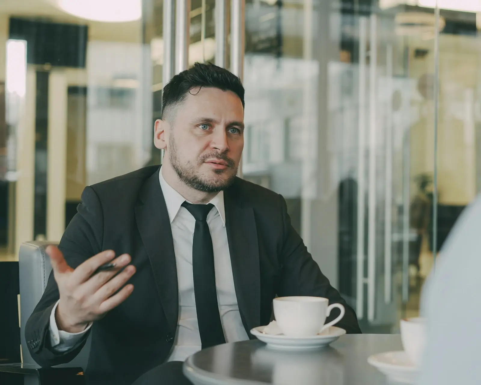 A lawyer in a dark suit explaining something to a client over coffee
