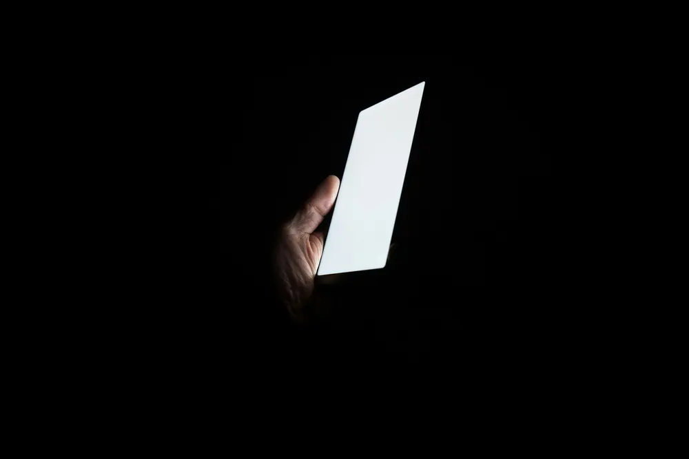 A hand holding a lit phone in a dark room