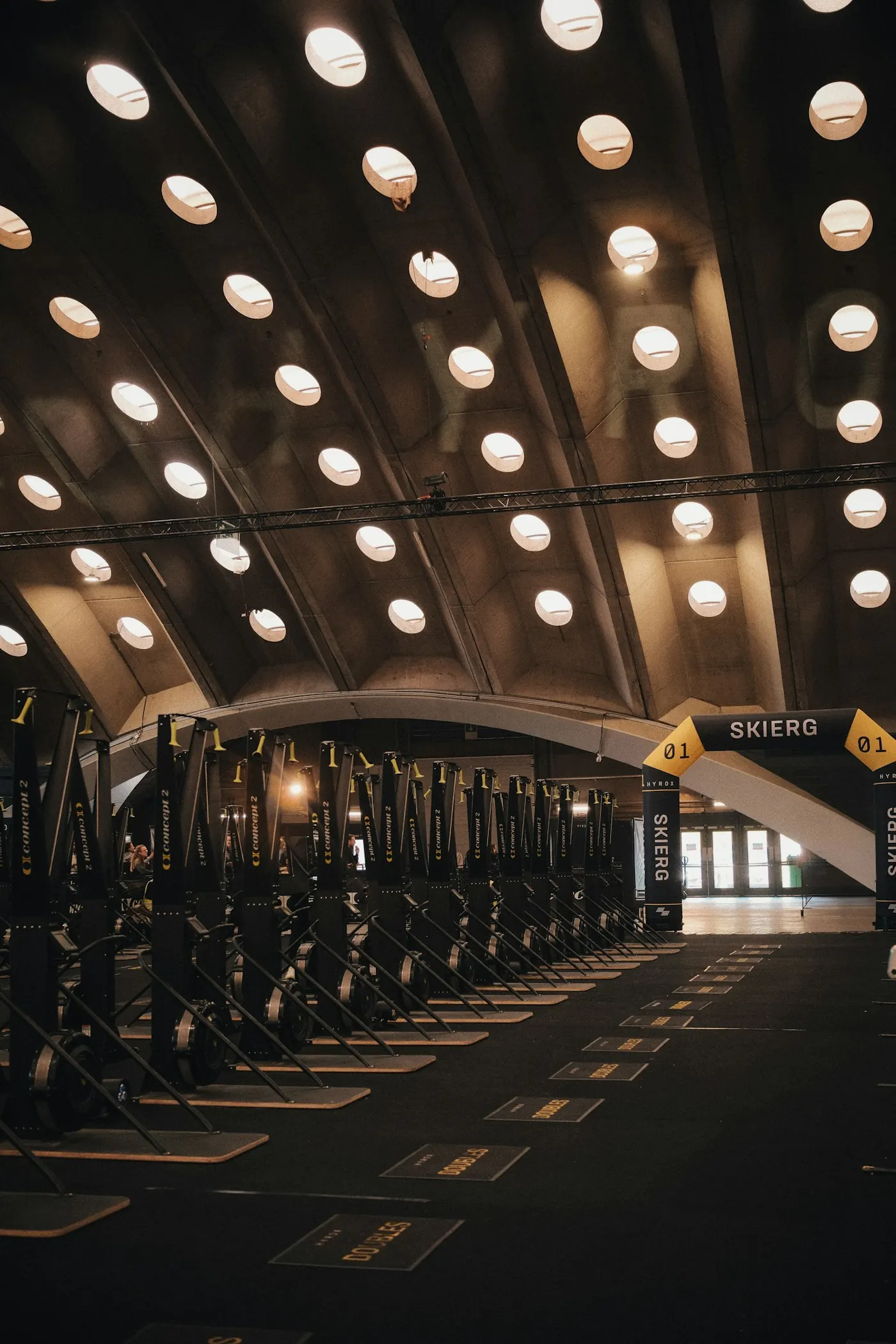 A long training hall with rows of ski machines under an arched ceiling of bulbs