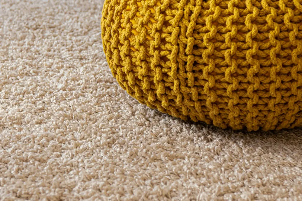 A beige carpet beside a knitted pouf