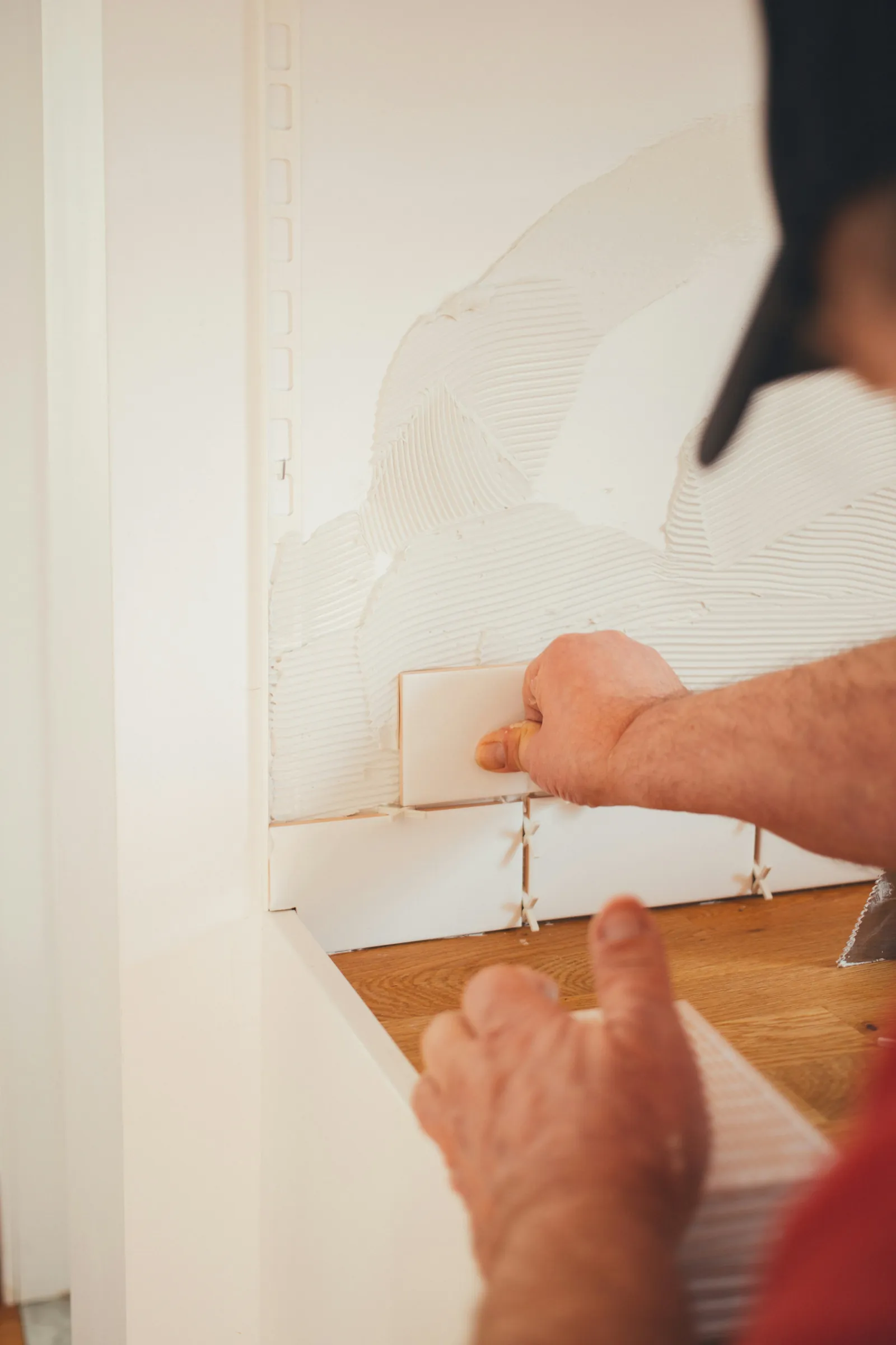 Hands fitting a plank of flooring against a white wall