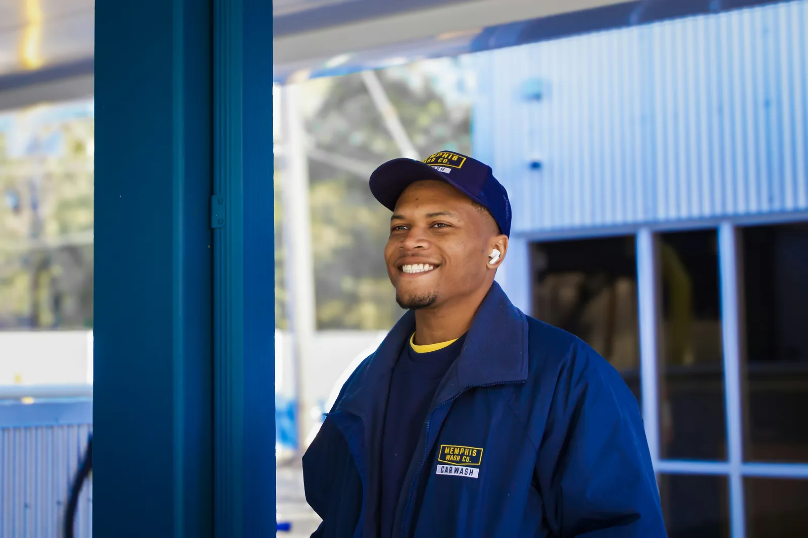 A smiling HVAC technician in a navy uniform and cap on a job