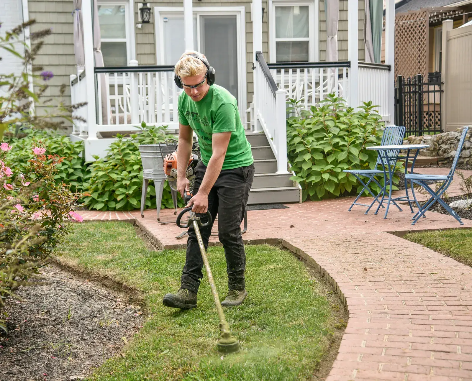 A landscaper edging the lawn along a brick path in front of a house