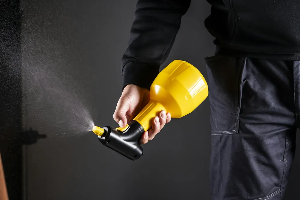 A hand holding a yellow sprayer against a dark background