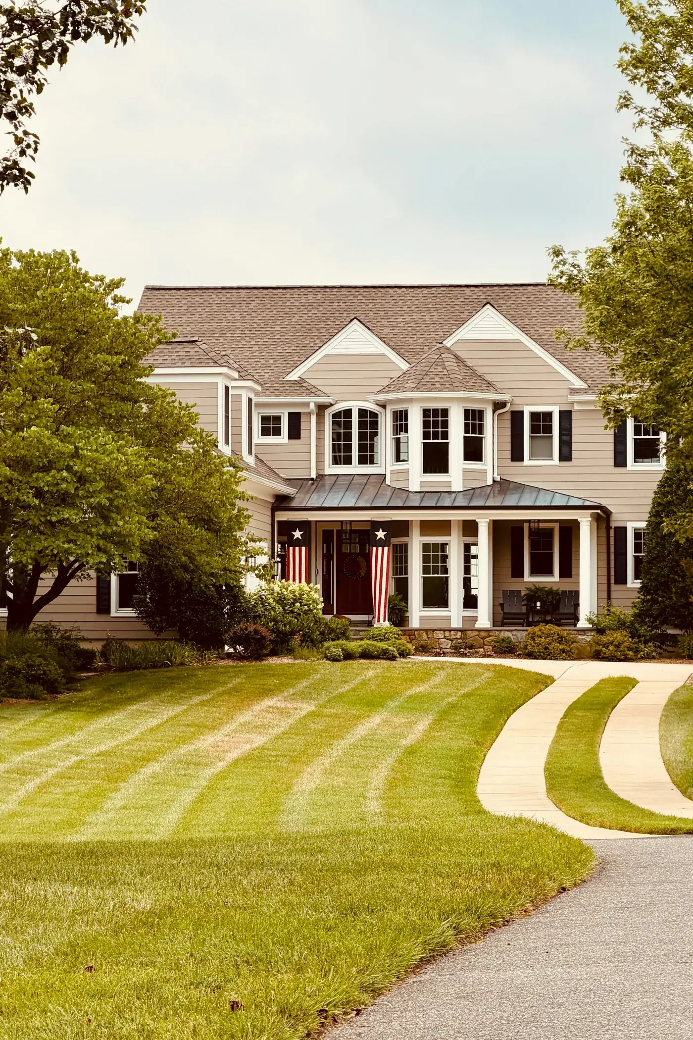 A two-storey house at the end of a curving driveway, behind a freshly striped lawn