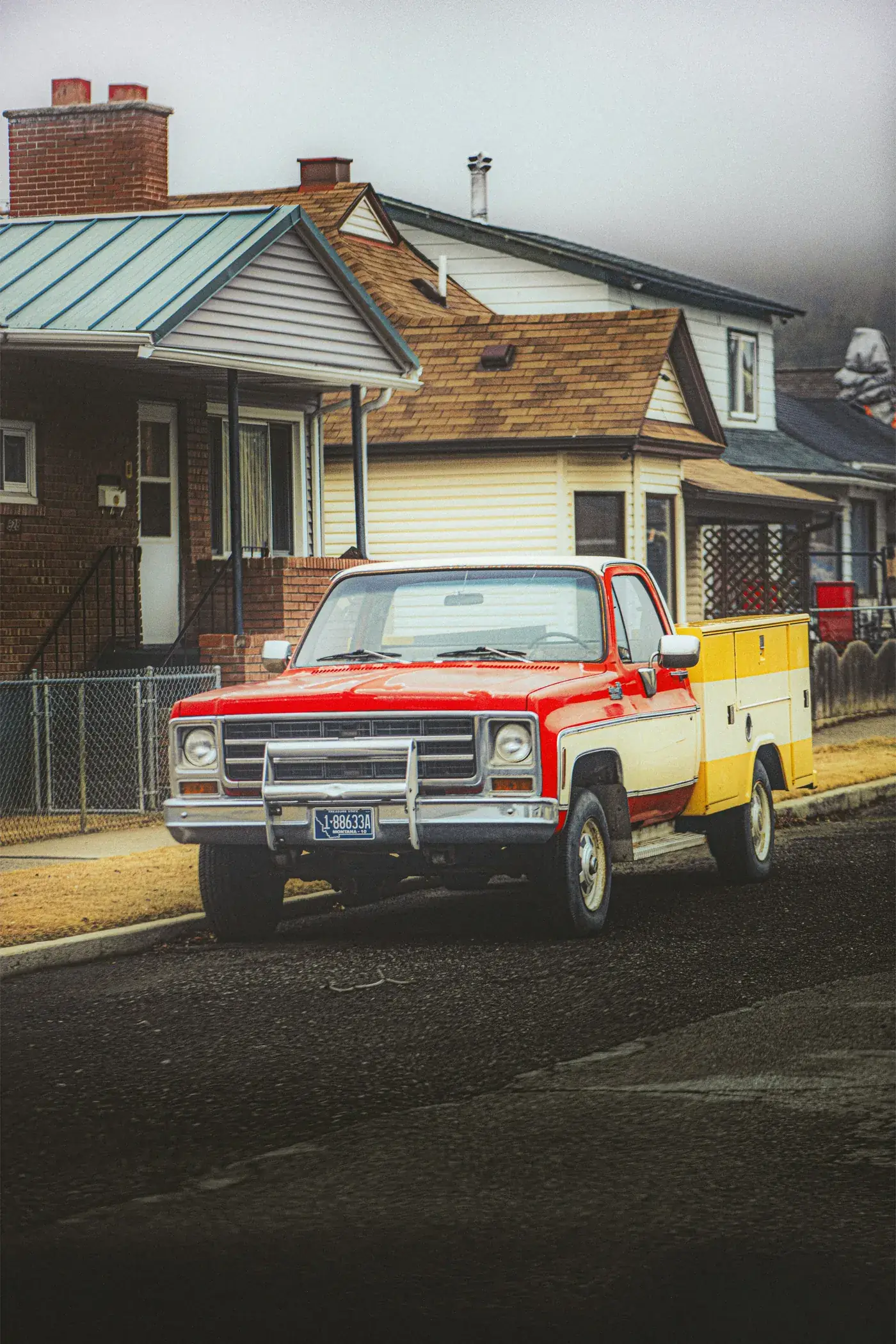 A red work pickup parked on a residential street outside a row of houses