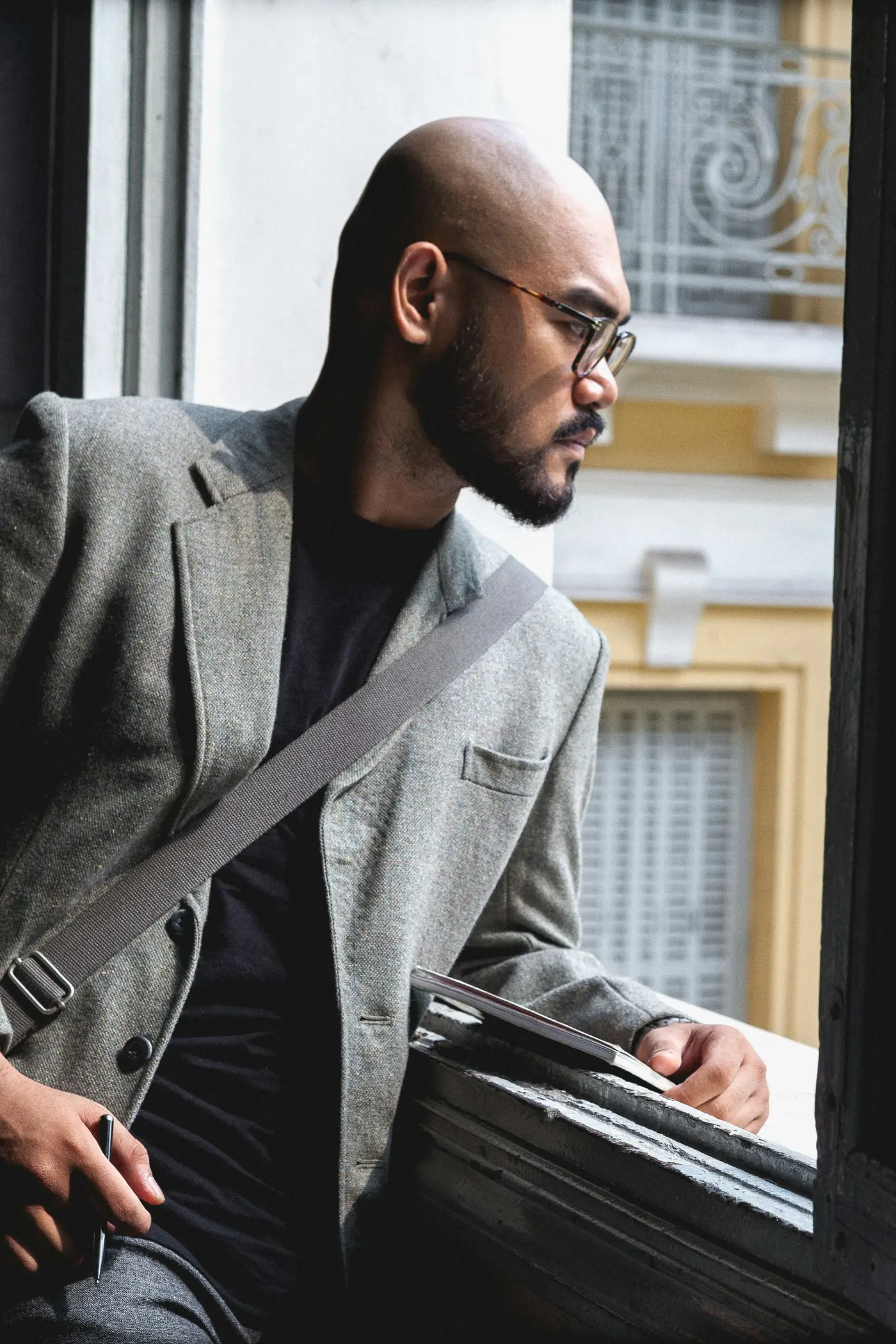 A man in a grey blazer sitting at an open window, looking out
