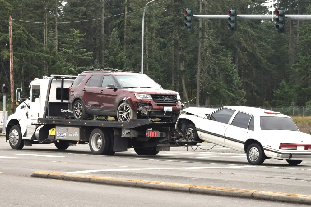 A tow truck hauling away two damaged cars at an intersection