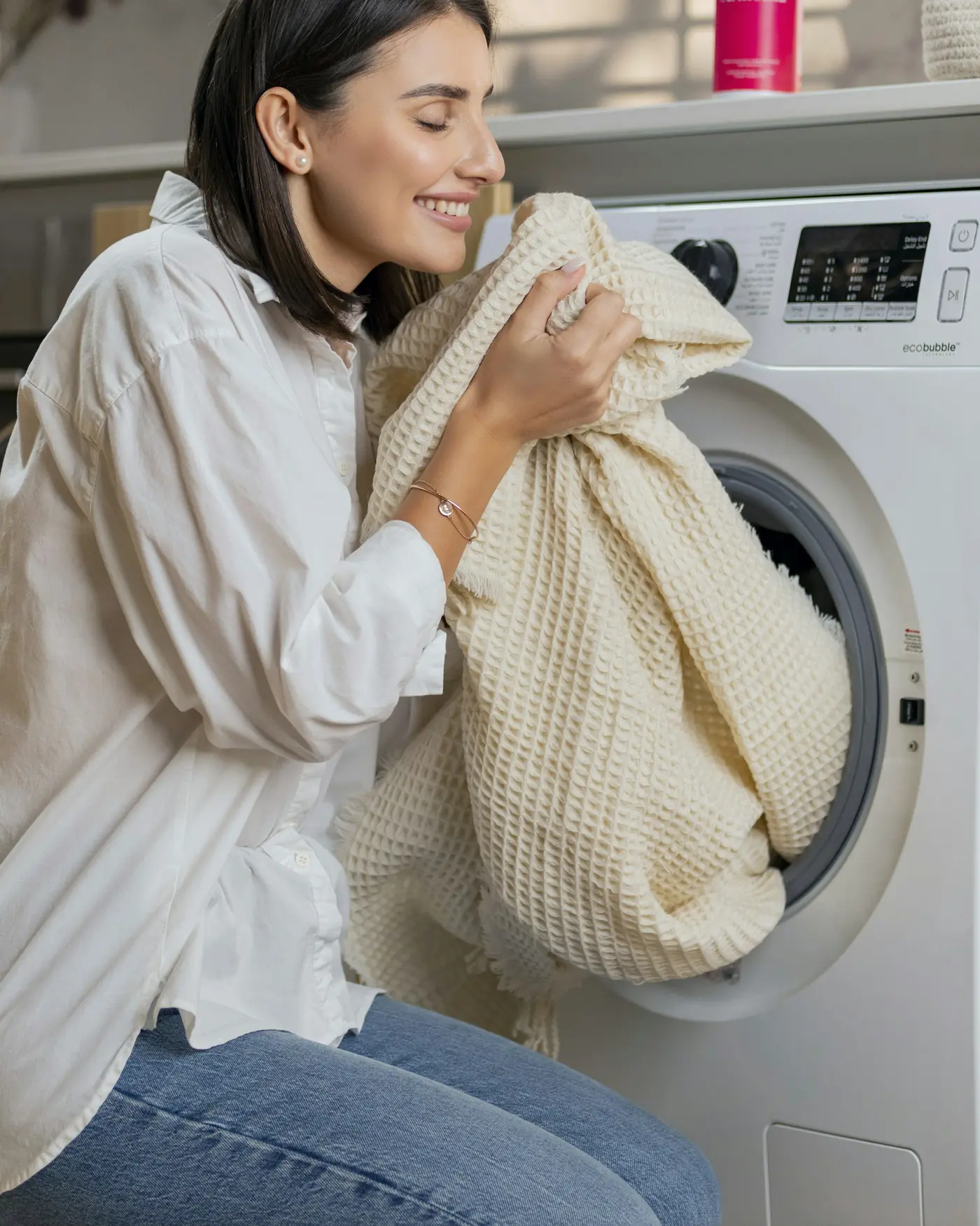 A woman holding a freshly washed blanket to her face beside a washer