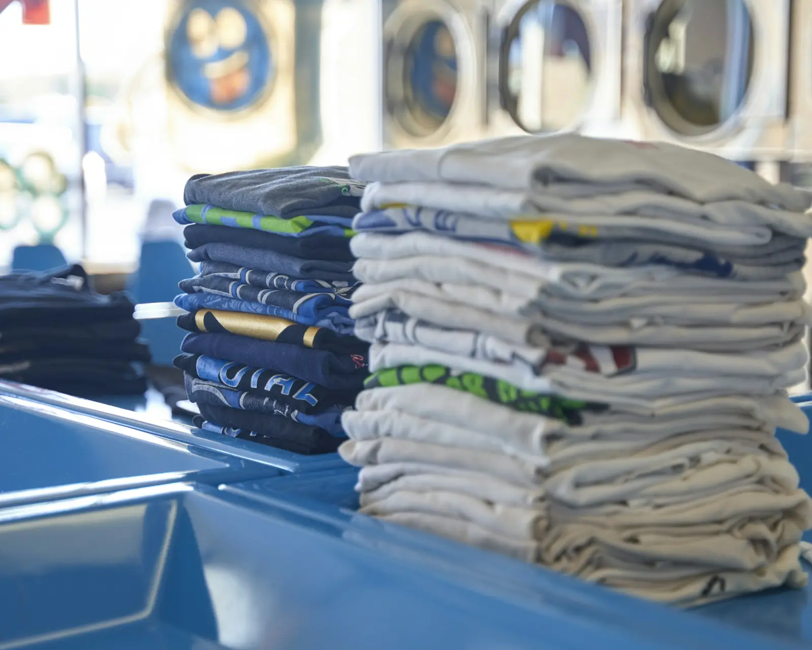 Stacks of folded shirts on a laundromat counter, washers behind
