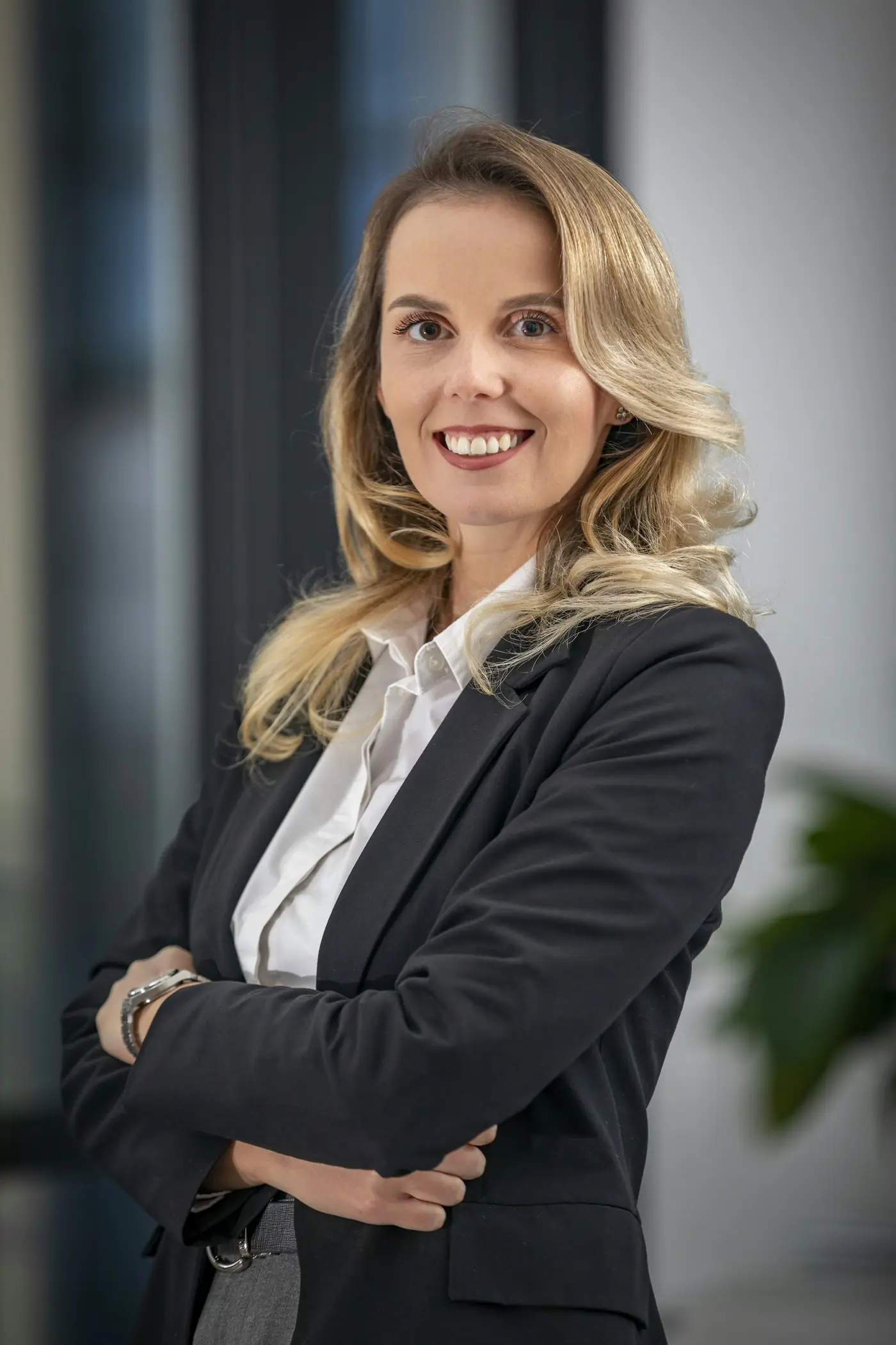 A lawyer in a dark blazer, arms folded, smiling in a bright office