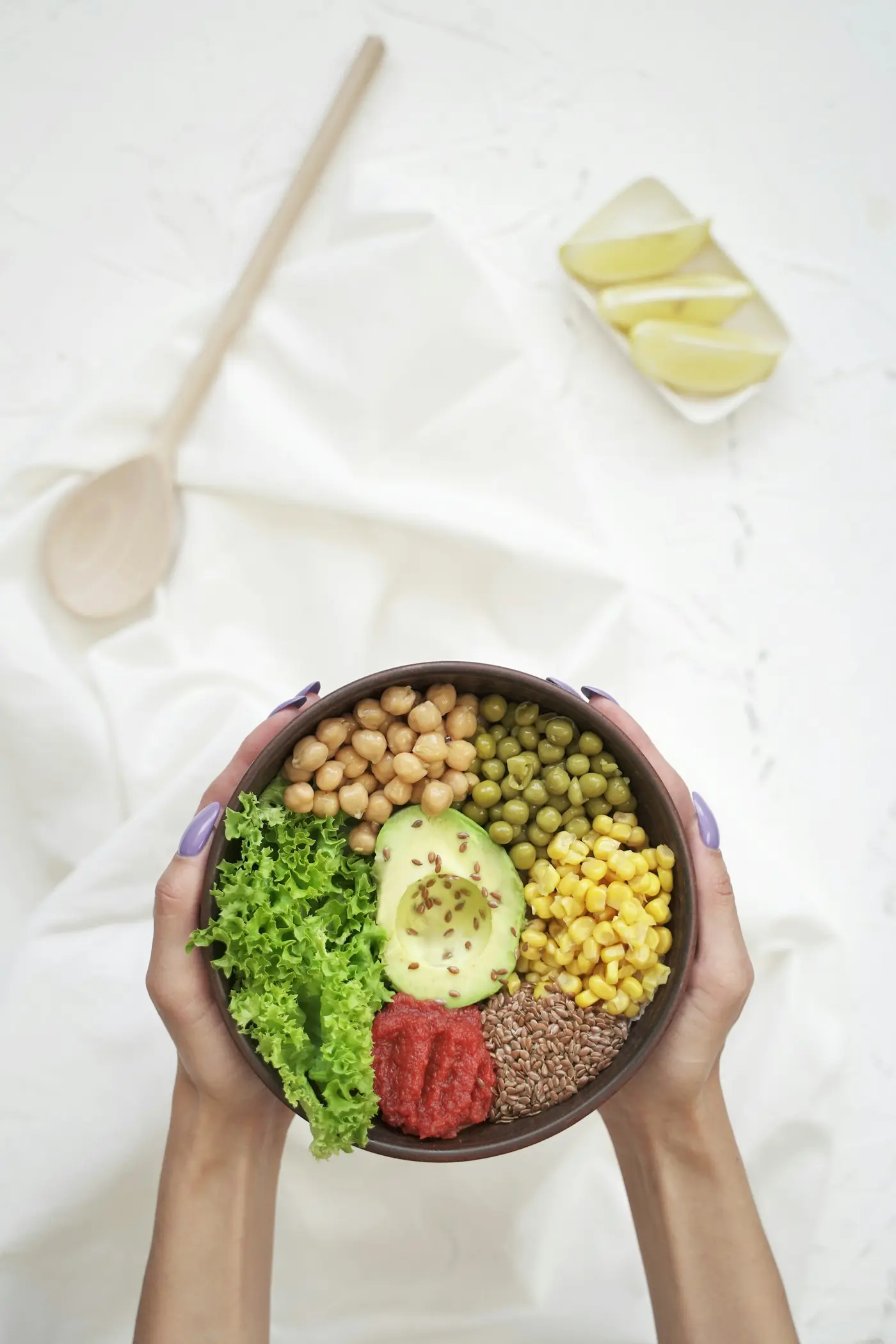 Two hands holding a bowl of chickpeas, avocado, corn and greens