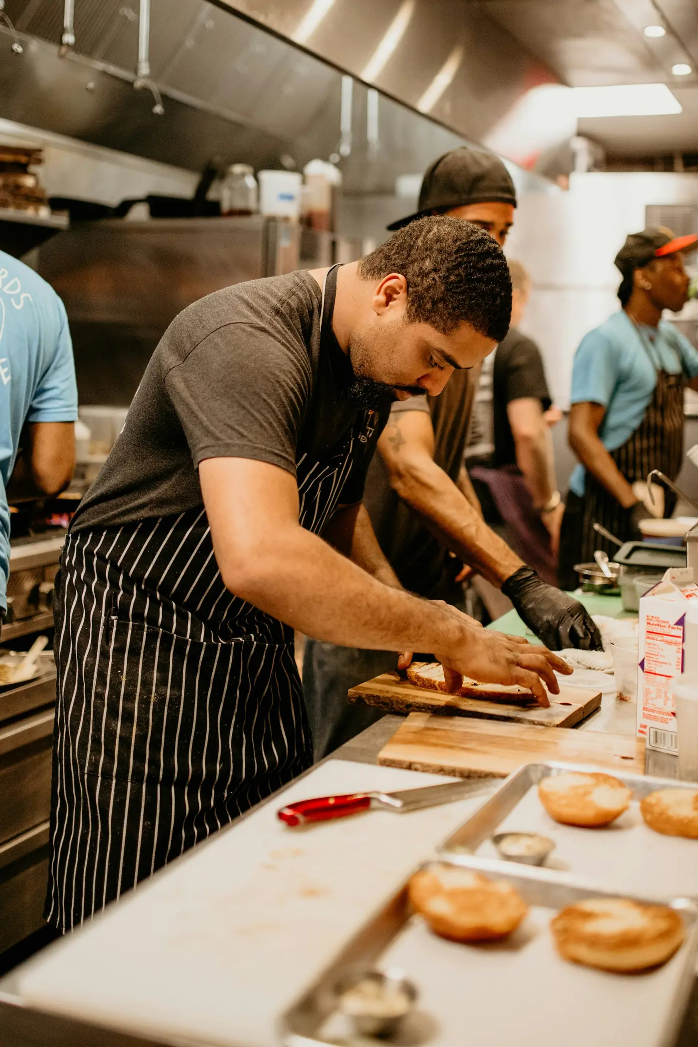 A cook in a striped apron prepping on a busy kitchen line