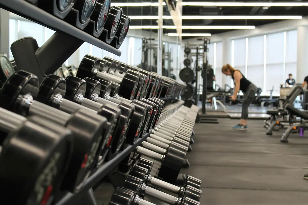 Racks of dumbbells in a bright gym with a few people training