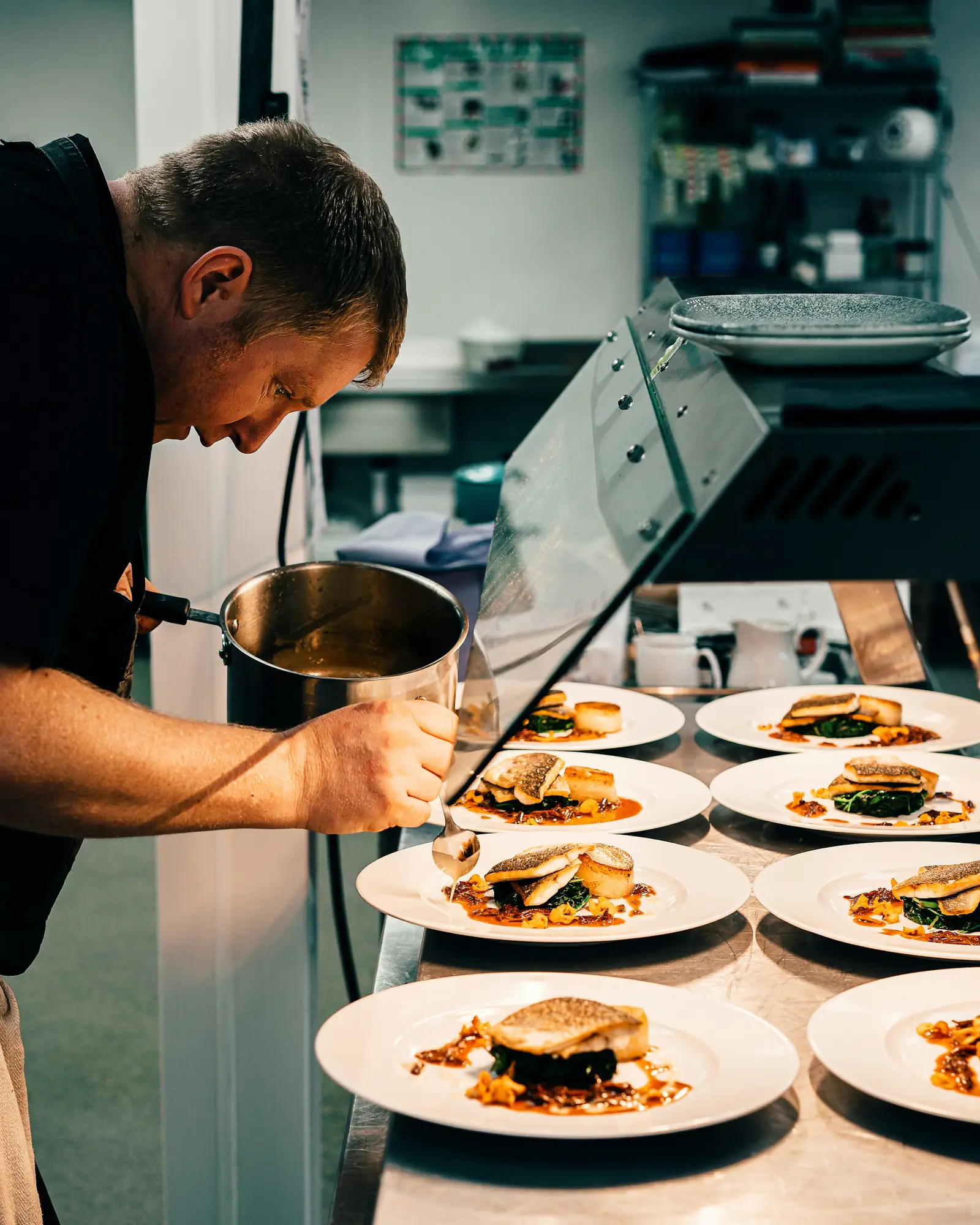 A chef finishing a row of plated meals on a steel pass