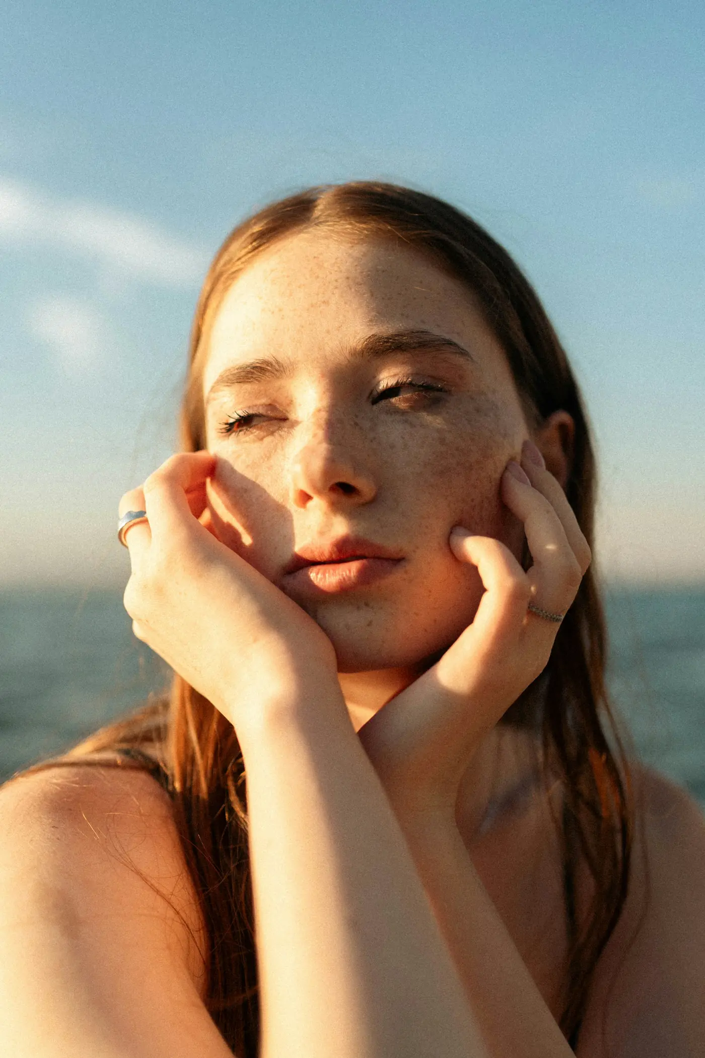 A woman with freckled skin resting her face in her hands in warm light