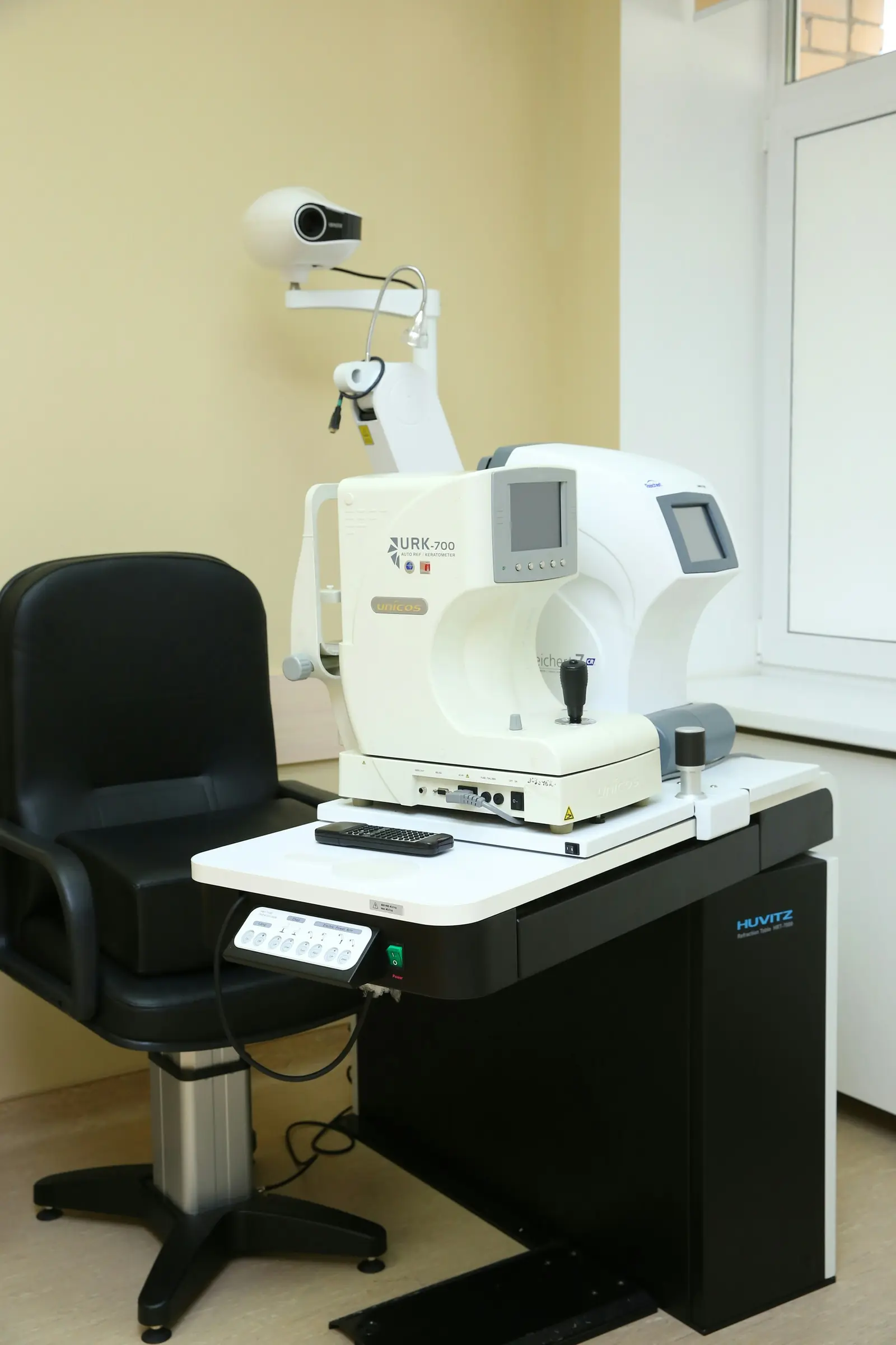 An exam chair beside an autorefractor in a bright exam room