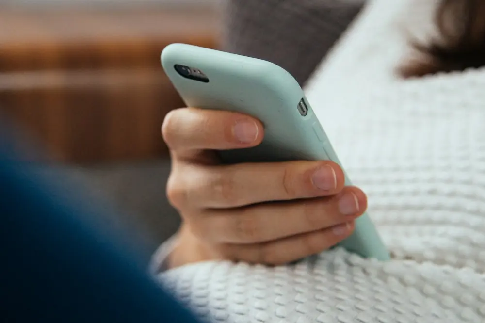 A hand holding a phone against a knitted blanket