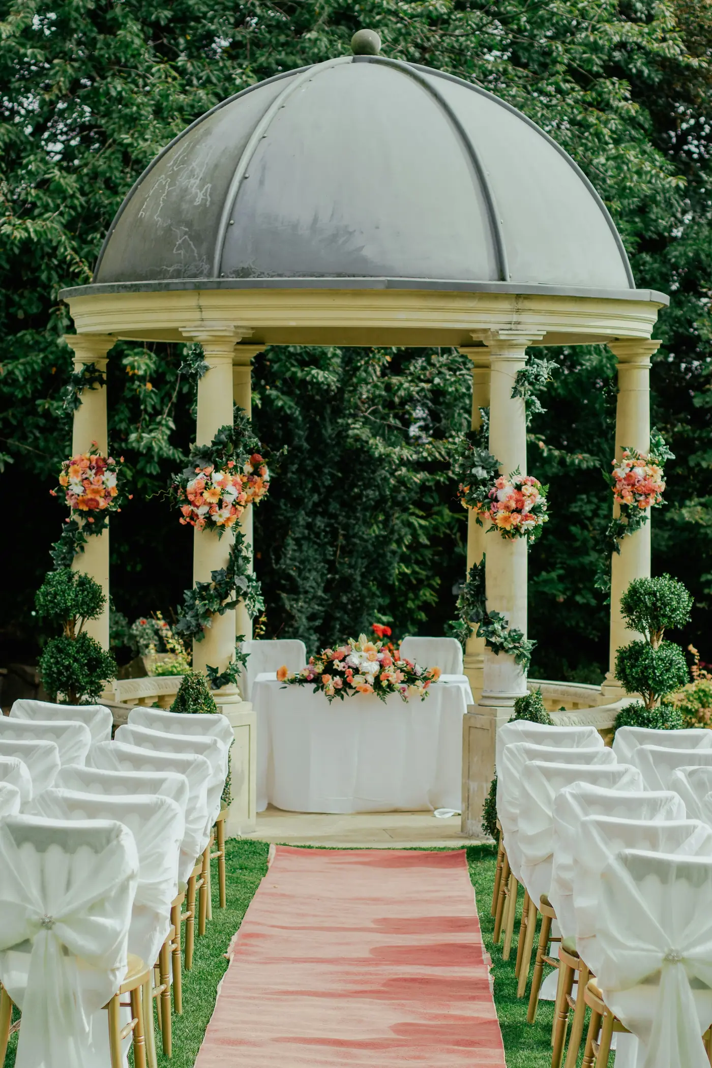 A garden ceremony set with white chairs under a gazebo