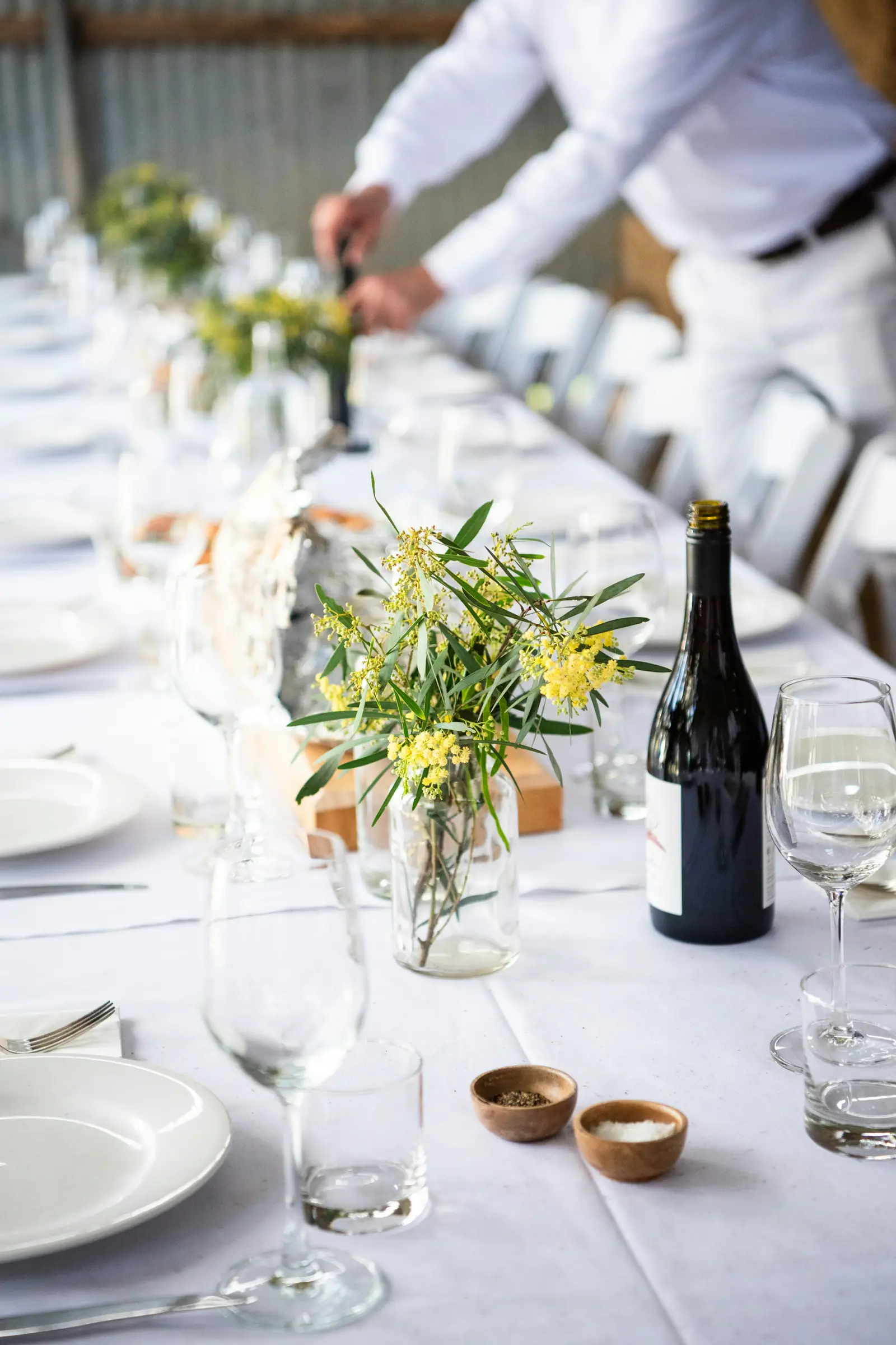 A planner setting a long table with flowers and glassware