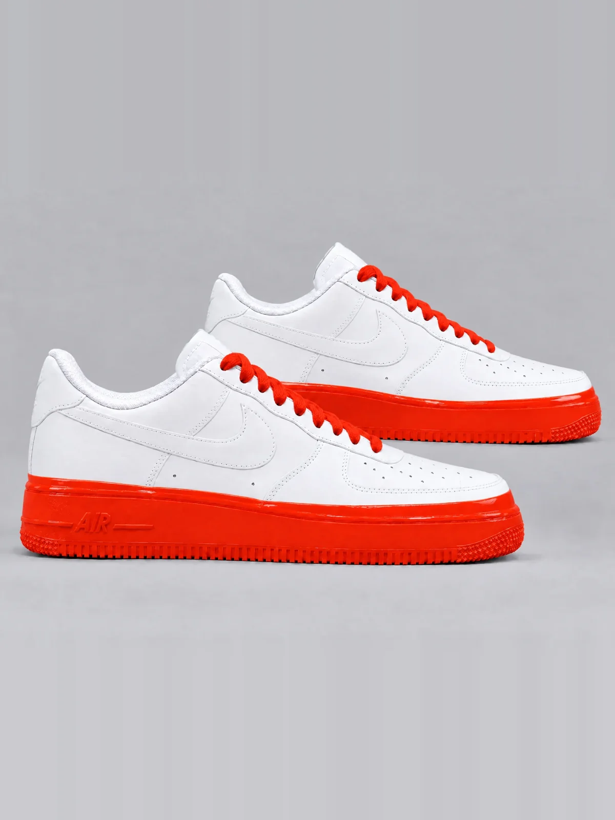 A pair of white leather low-top sneakers with orange cotton laces, their soles dipped in glossy orange paint up to a clean, level line