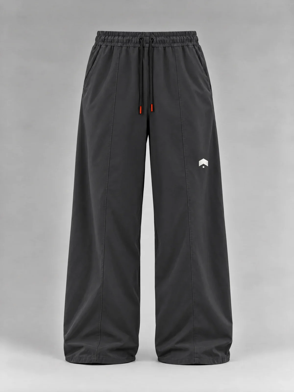 Dark grey wide-leg pants with an elastic waist, a black drawcord with orange tips and a seam down each leg, our mark small in white above the left knee