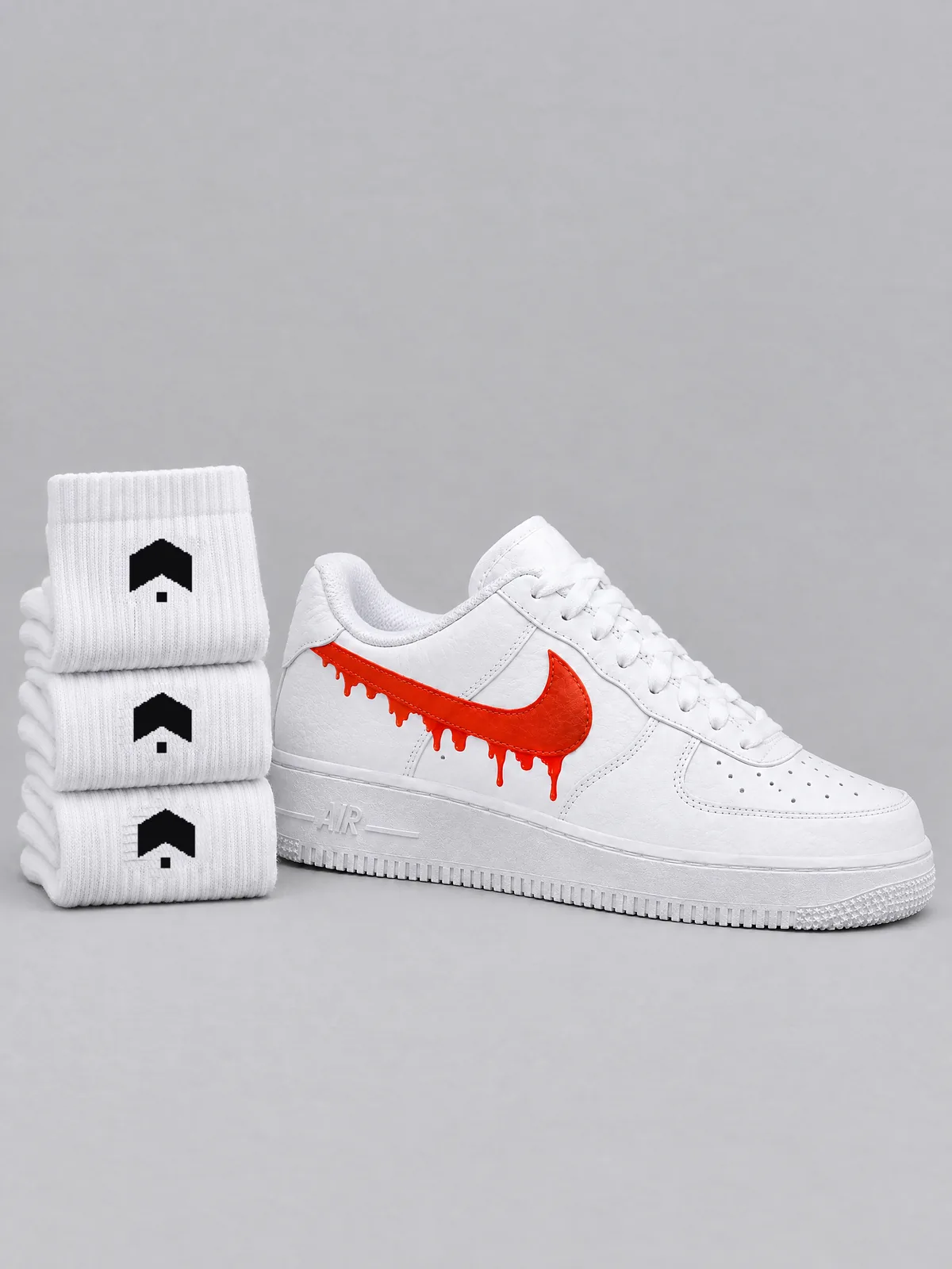 Three pairs of white crew socks folded in a stack, each with our mark knitted in black, beside a white sneaker with an orange dripping side logo