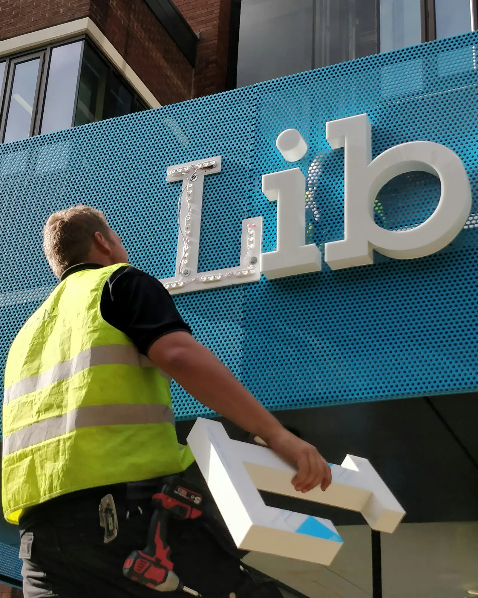 An installer in a high-visibility vest fitting letters to a building fascia