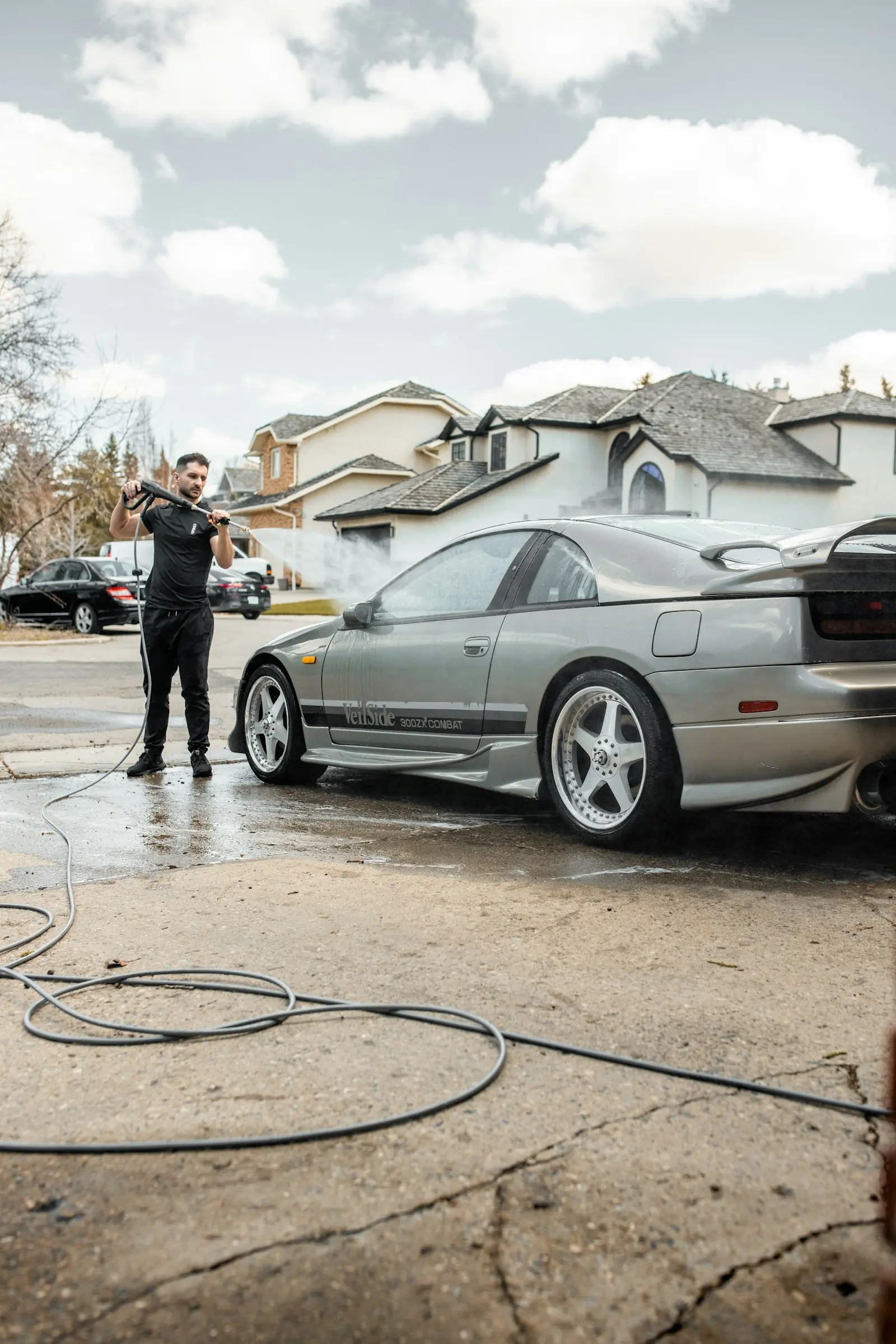 A detailer rinsing a silver car on a residential street