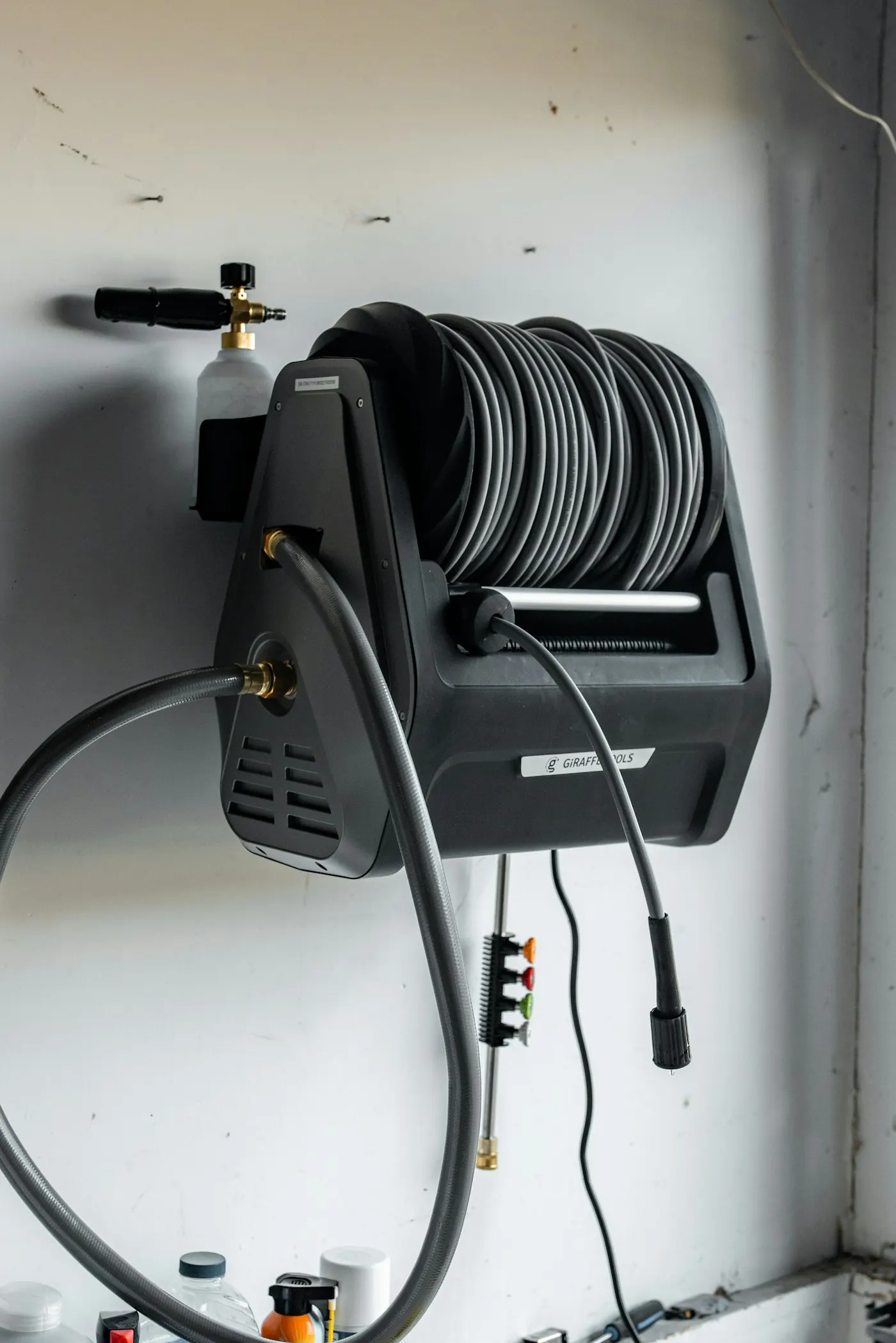 A pressure washer hose reel and foam cannon mounted on a wall