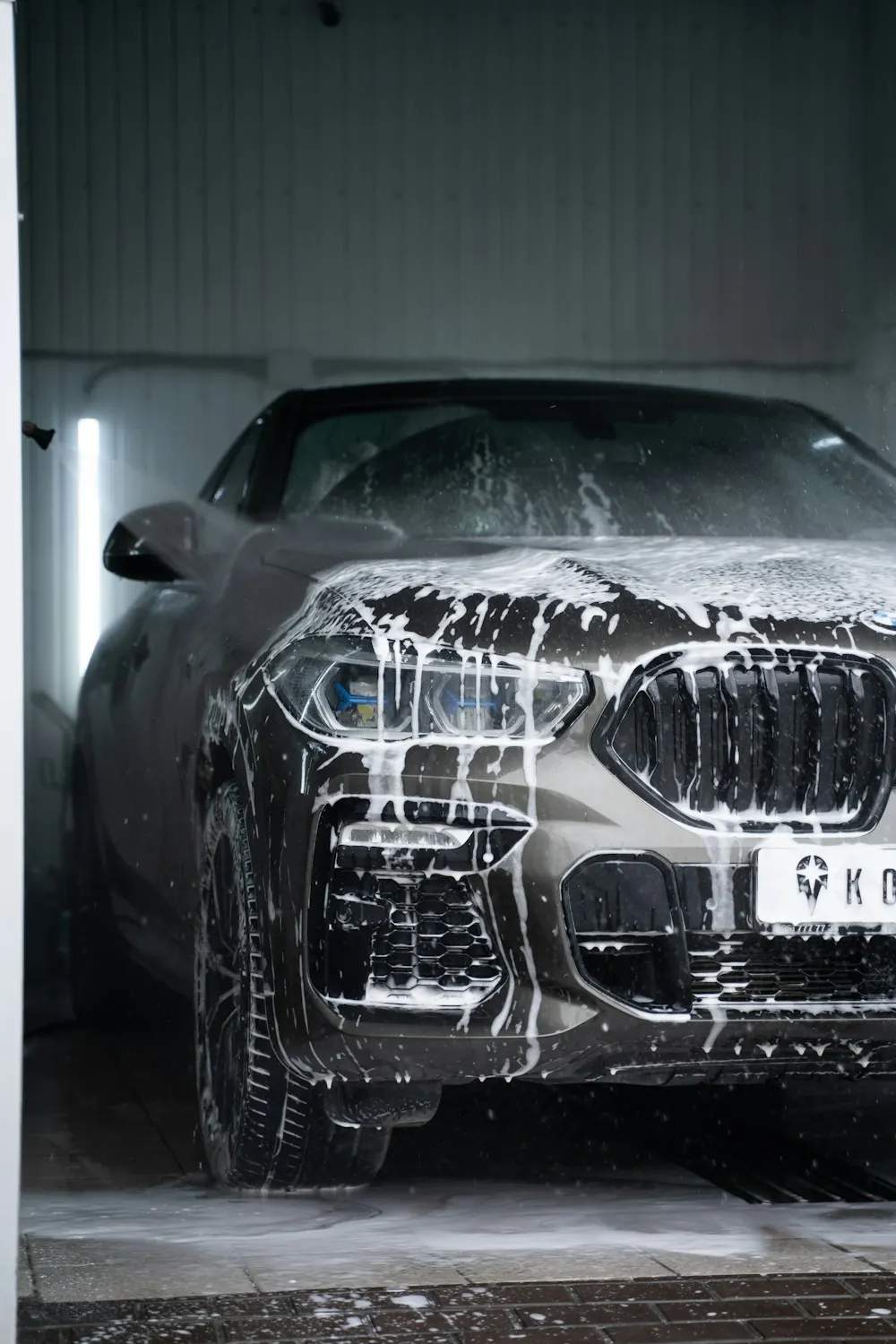 A grey SUV covered in foam in a wash bay