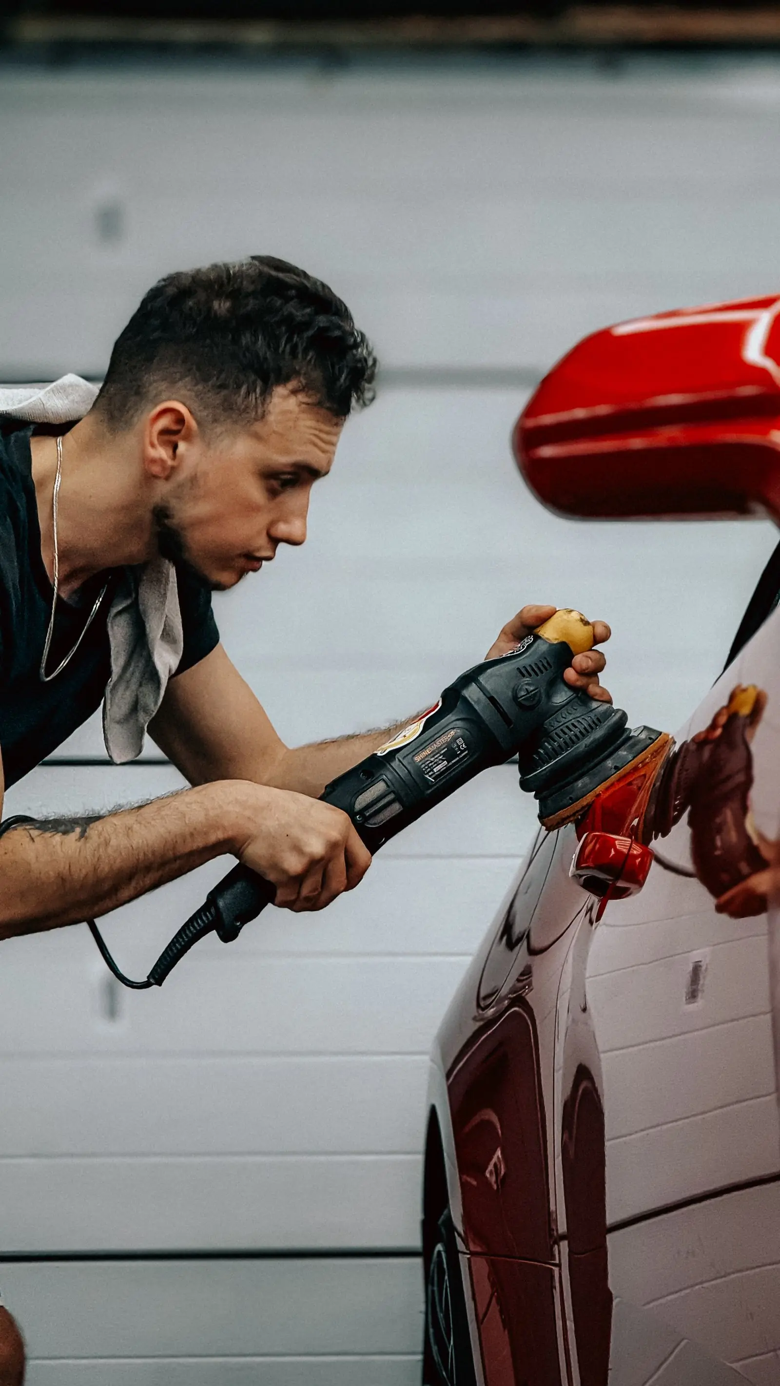 A detailer running a machine polisher over a red car
