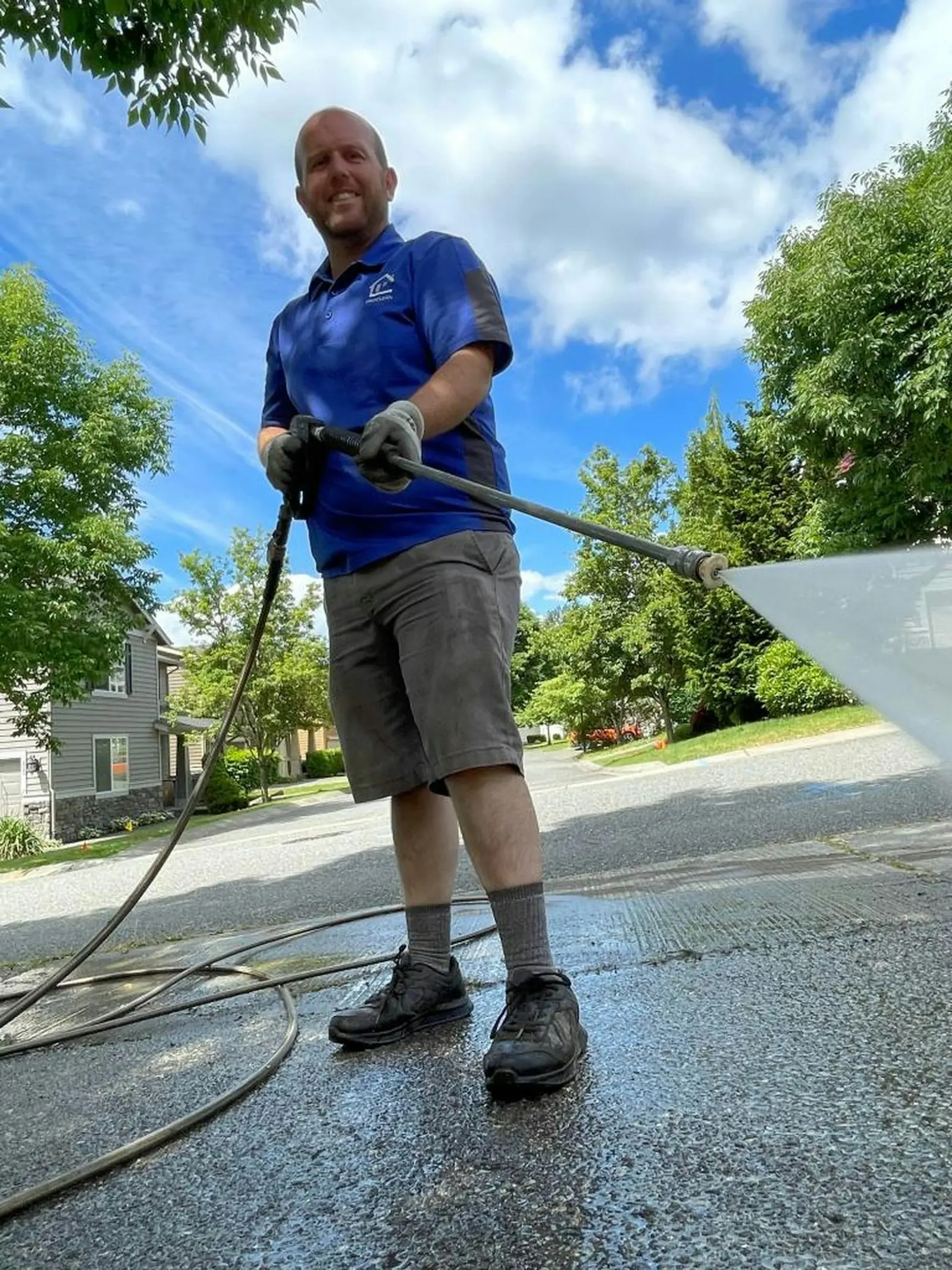 A pressure washing contractor cleaning a driveway on a sunny residential street