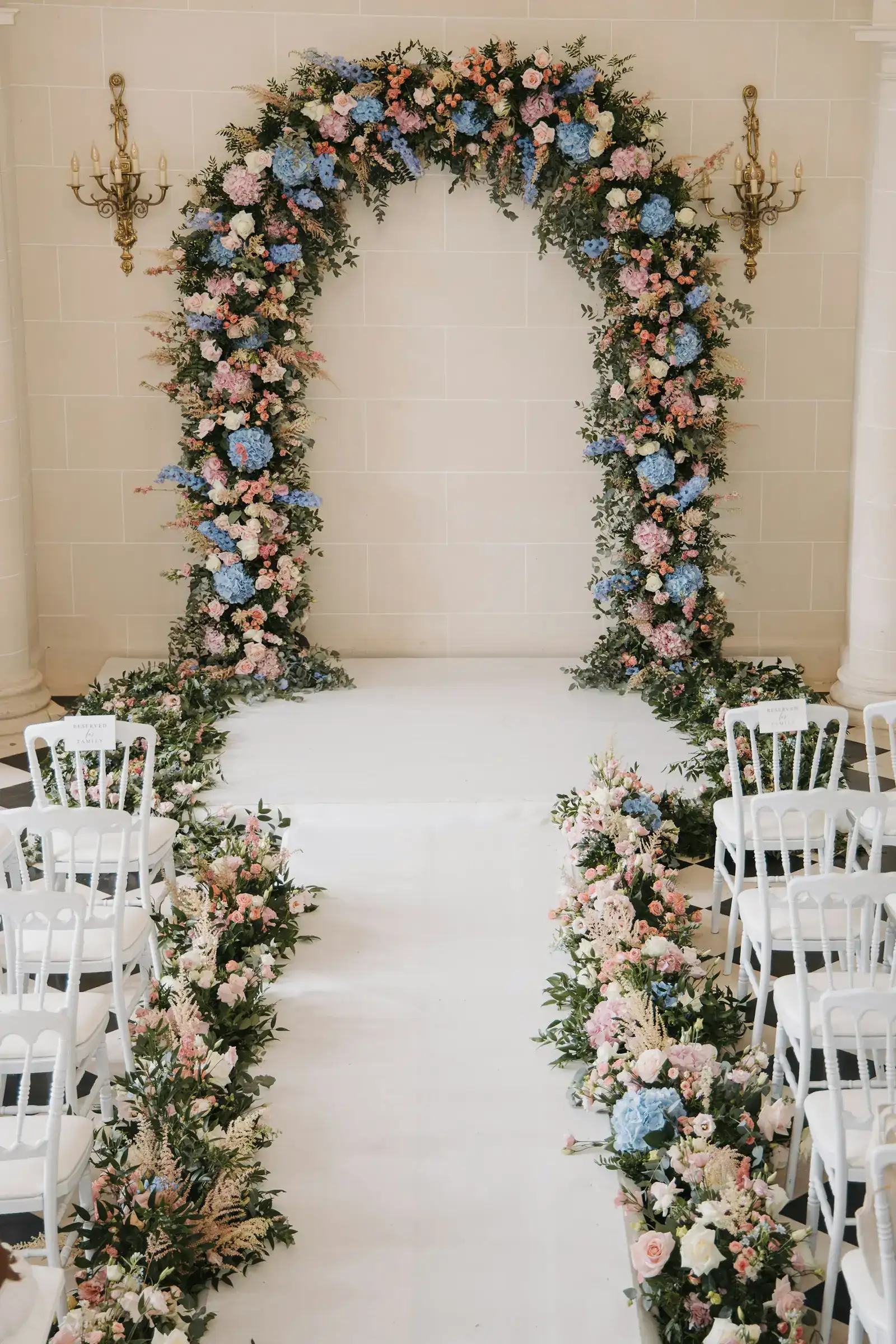 A floral arch over an aisle lined with white chairs
