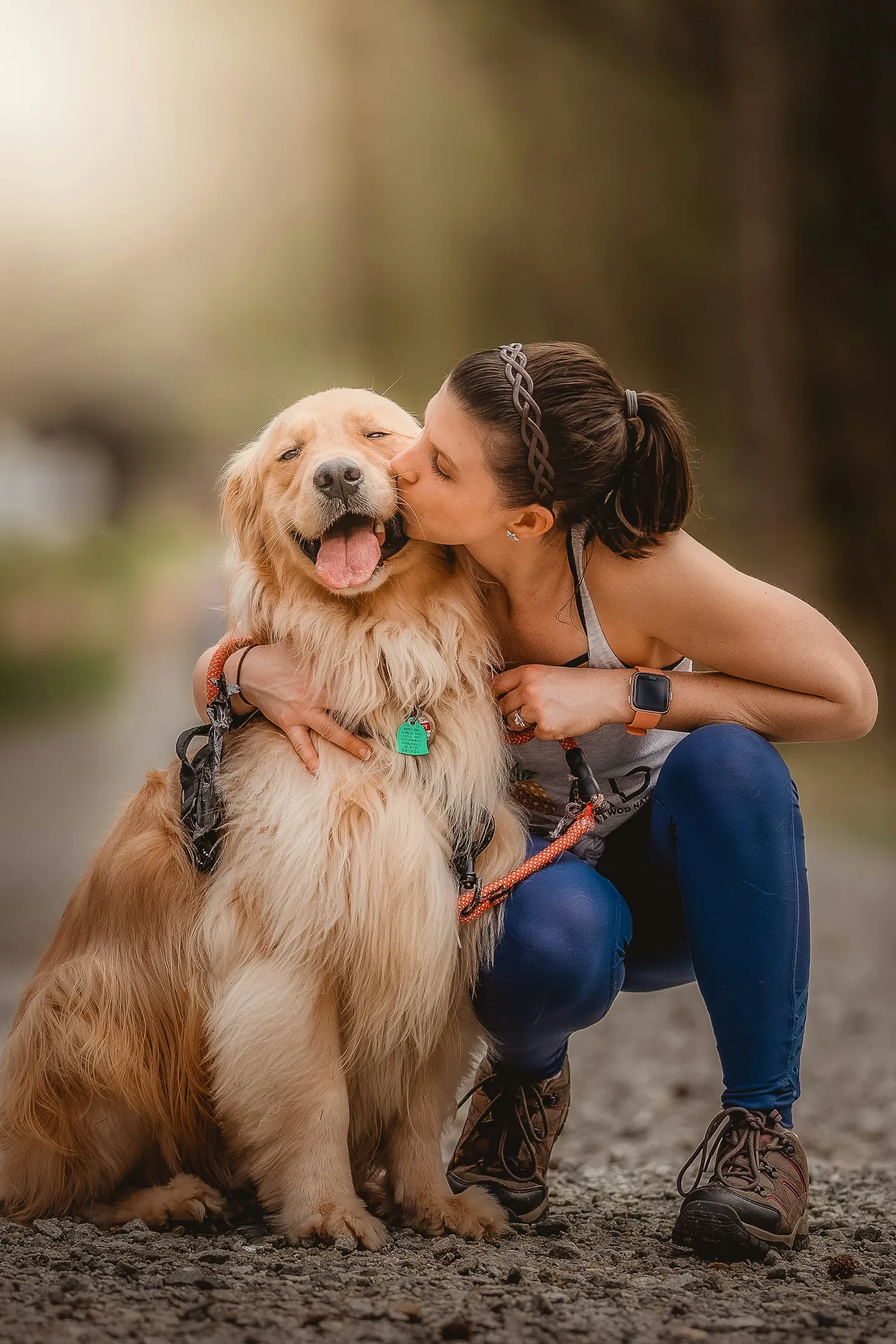 A woman kneeling on a path hugging a golden retriever