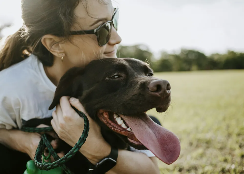 A woman hugging her black dog outdoors
